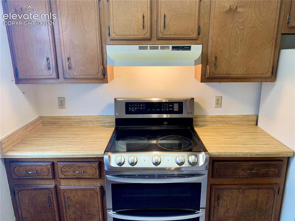 Image 7 of 18: Stainless steel range with a glass cooktop, wood-finish countertops, wood u