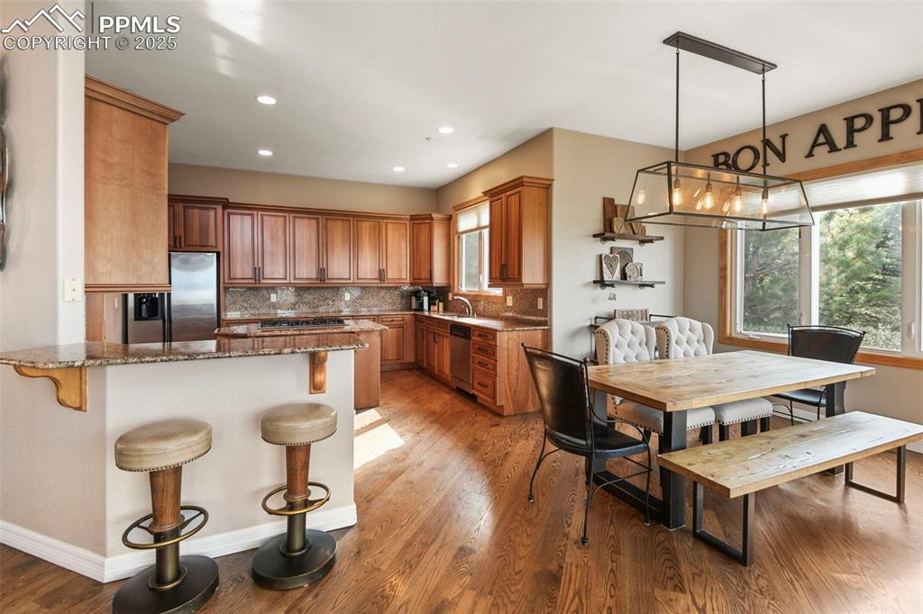 Image 10 of 39: Kitchen featuring dark stone counters, a breakfast bar area, brown cabinetr