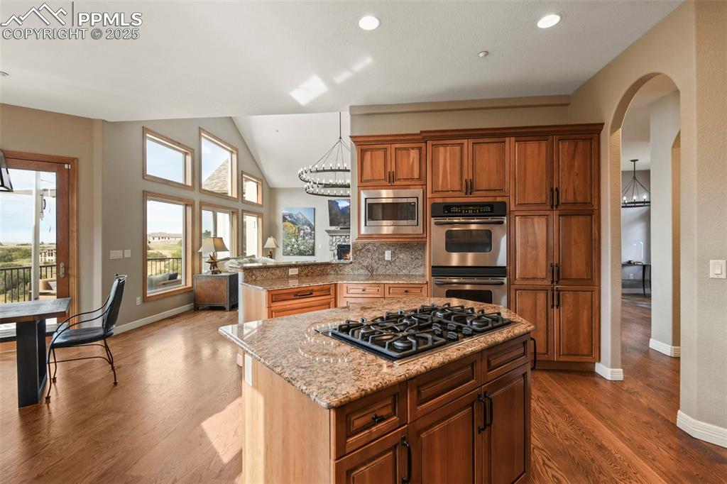 Image 12 of 39: Kitchen featuring arched walkways, light stone countertops, appliances with