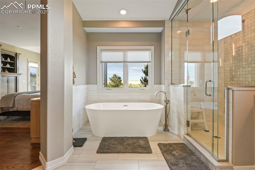 Image 15 of 39: Ensuite bathroom featuring tile walls, a freestanding bath, a stall shower,