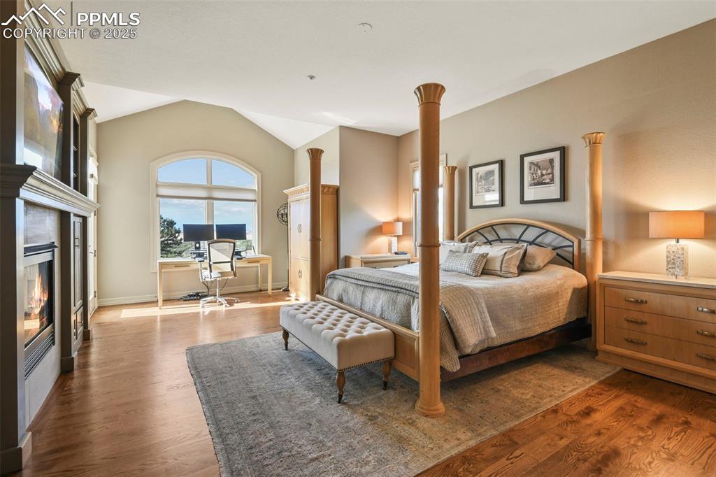 Image 19 of 39: Bedroom with dark wood-style flooring, a glass covered fireplace, lofted ce