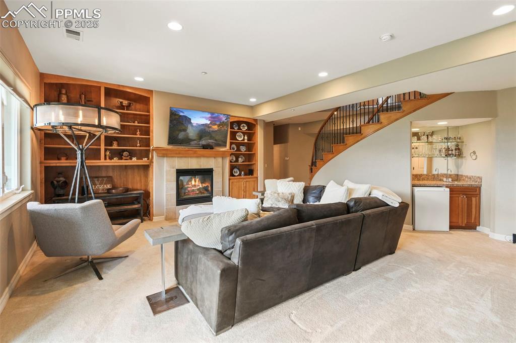Image 23 of 39: Living area with built in features, a fireplace, stairway, wet bar, and rec
