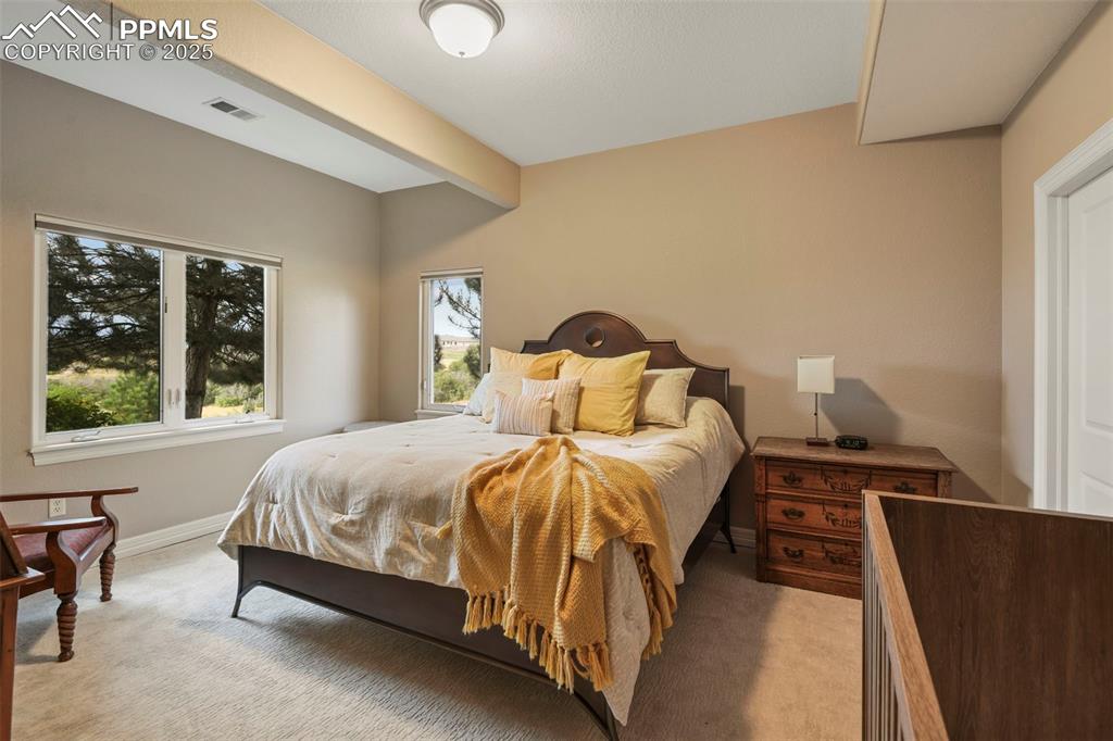 Image 32 of 39: Bedroom with beamed ceiling and light carpet