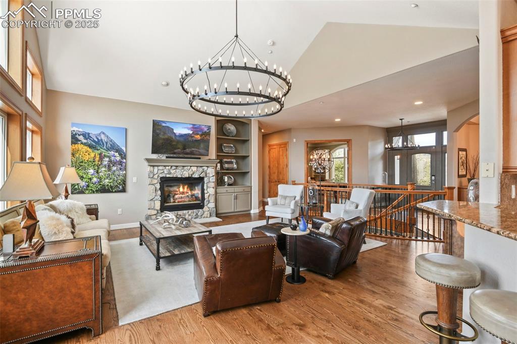Image 5 of 39: Living area featuring a stone fireplace, wood finished floors, a chandelier