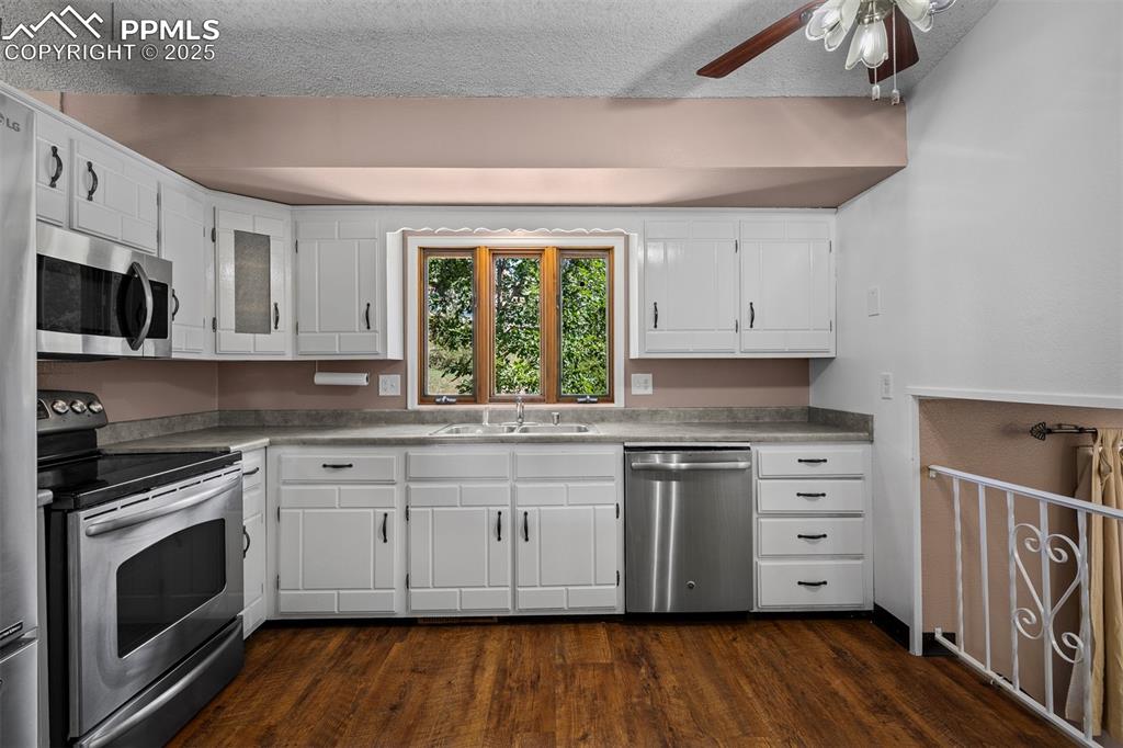 Image 27 of 49: Kitchen with stainless steel appliances, white cabinetry, dark wood-style f