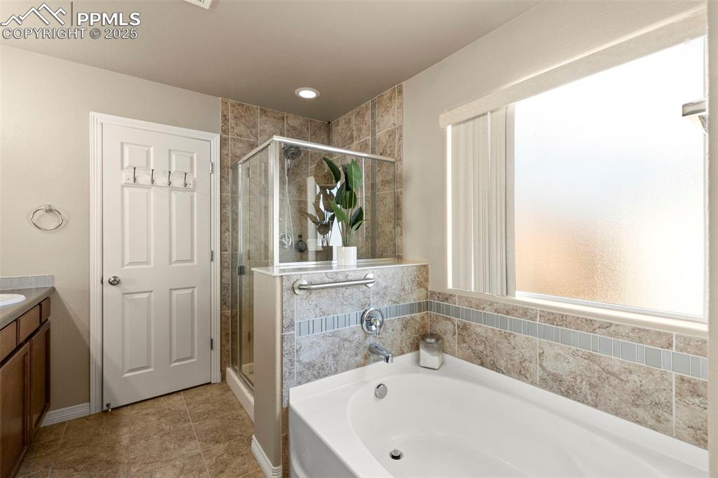 Image 19 of 27: Full bath featuring a garden tub, a stall shower, vanity, and tile patterne