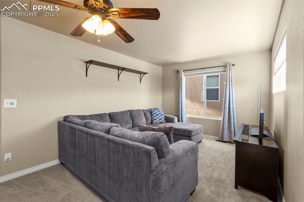 Image 22 of 27: Living room with light colored carpet and a ceiling fan
