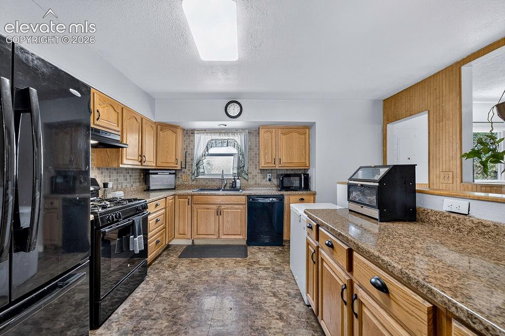 Image 22 of 44: Kitchen featuring wood-finish cabinetry, speckled countertops, and a tile b