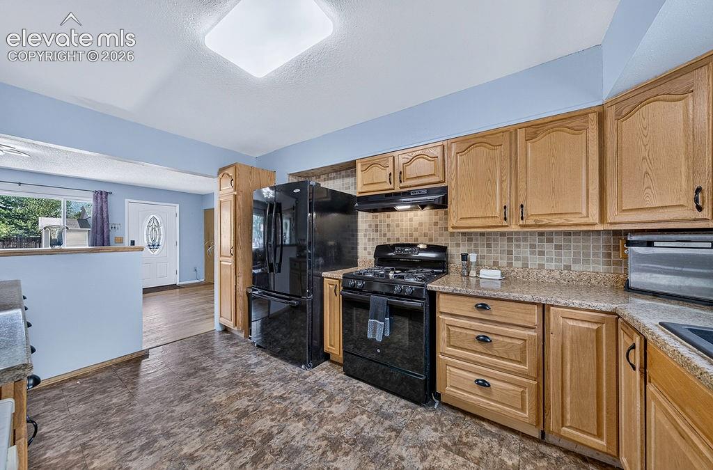 Image 40 of 44: Kitchen featuring wood cabinetry, a mosaic tile backsplash, and a black app