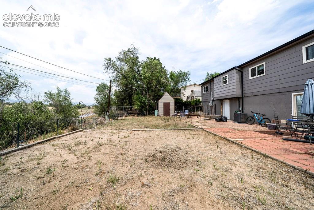 Image 9 of 44: Expansive backyard featuring a red brick patio, a two-story shed, and matur