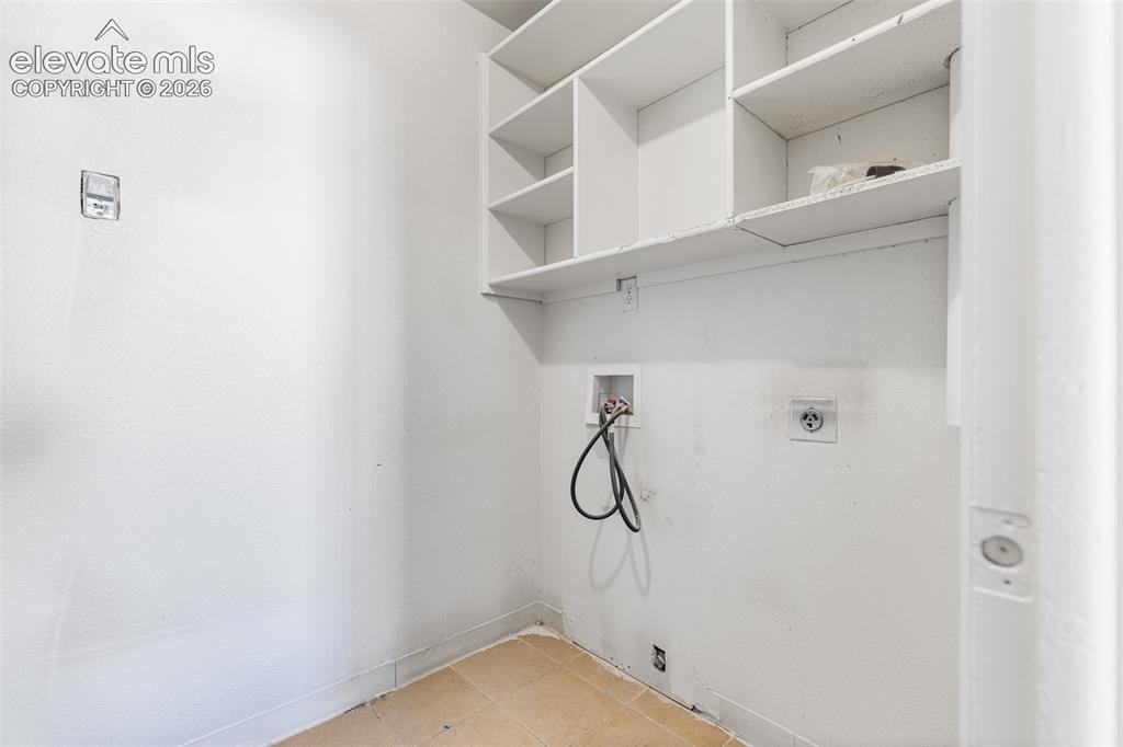 Image 17 of 19: Utility room featuring white shelving, tiled flooring, and appliance hookup