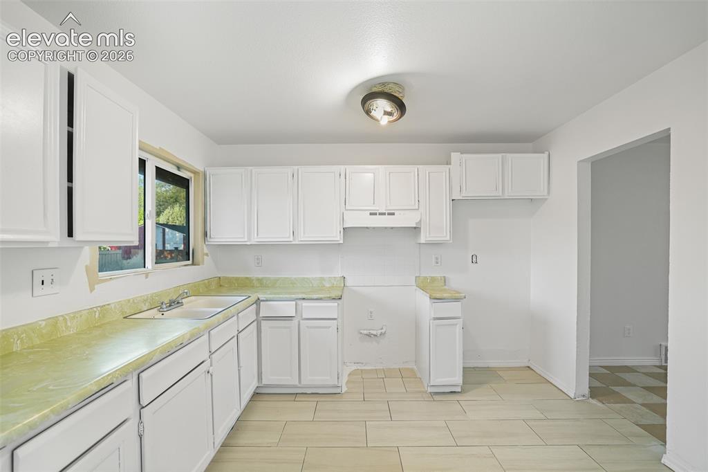 Image 7 of 19: Bright kitchen featuring white cabinetry and light-toned flooring