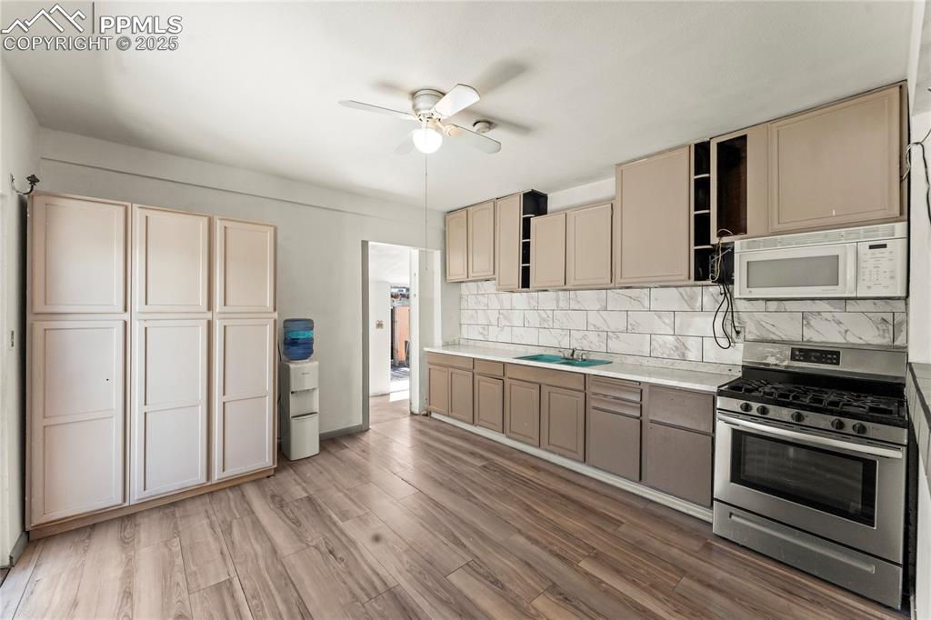 Image 9 of 36: Kitchen with white microwave, a ceiling fan, stainless steel range with gas