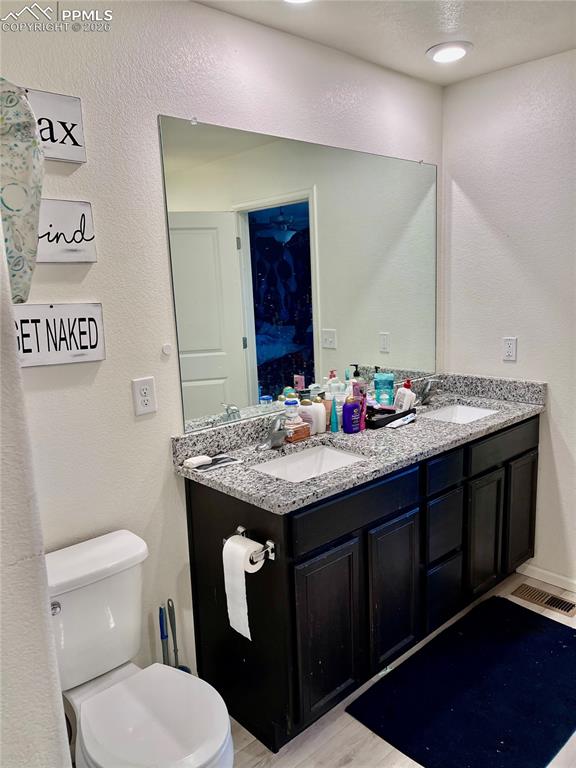 Image 11 of 17: Full bathroom with a textured wall, double vanity, and light wood-type floo