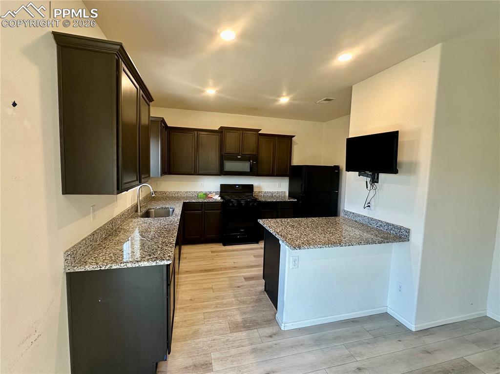 Image 7 of 17: Kitchen featuring light stone counters, dark brown cabinetry, black applian