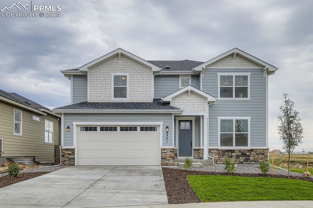 Caption: Craftsman-style home featuring stone siding, driveway, a garage, and a shingled roof