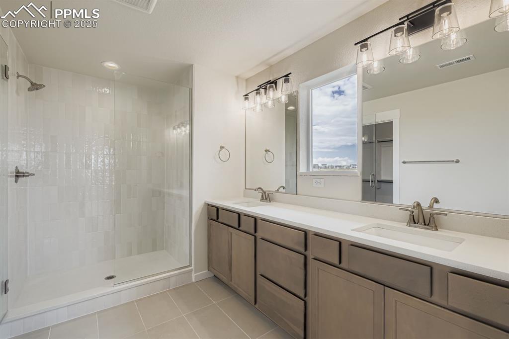 Image 15 of 28: Full bathroom with double vanity, light tile patterned floors, a shower sta