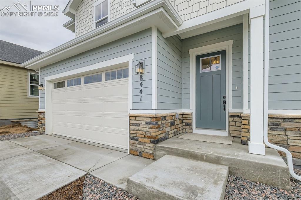 Image 3 of 28: Property entrance featuring stone siding, concrete driveway, and an attache