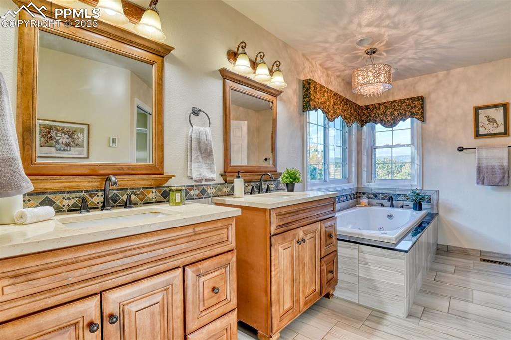 Image 30 of 44: Bathroom with a tub with jets, two vanities, a chandelier, and a textured w