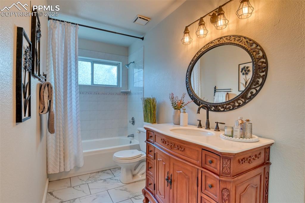 Image 33 of 44: Bathroom with shower / bath combo, vanity, a textured wall, and light marbl
