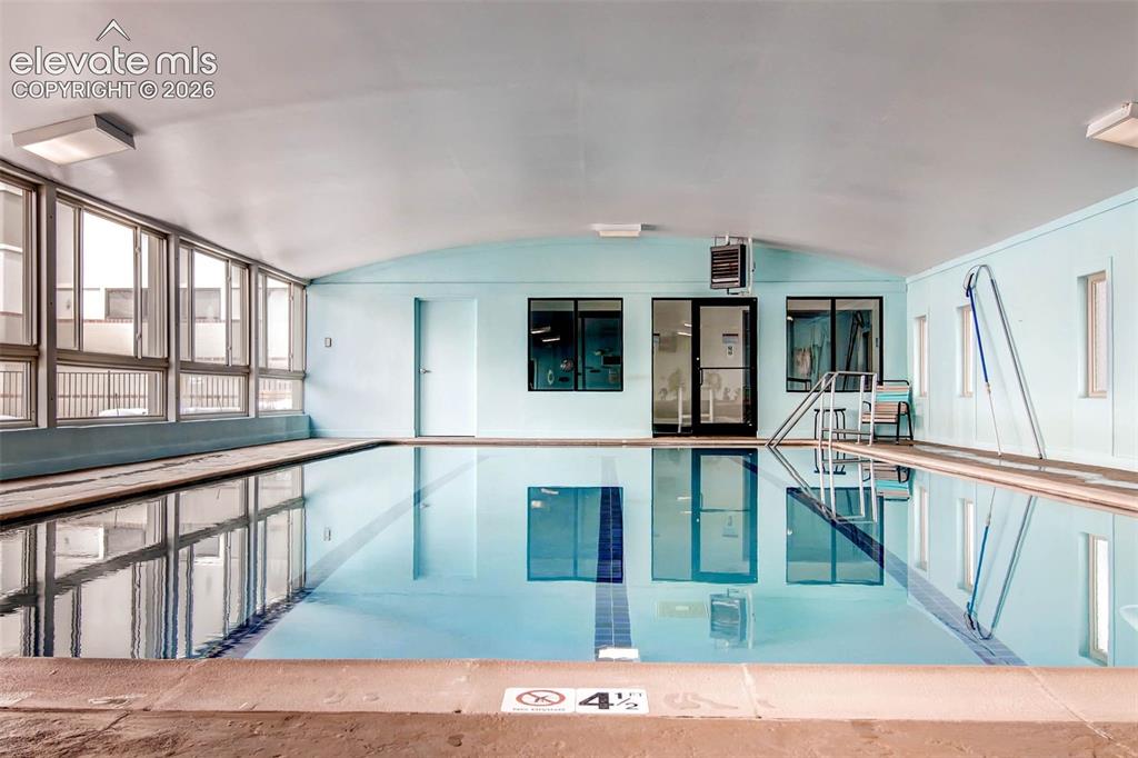 Image 17 of 27: Indoor swimming pool featuring a curved ceiling, full-height windows, a gla
