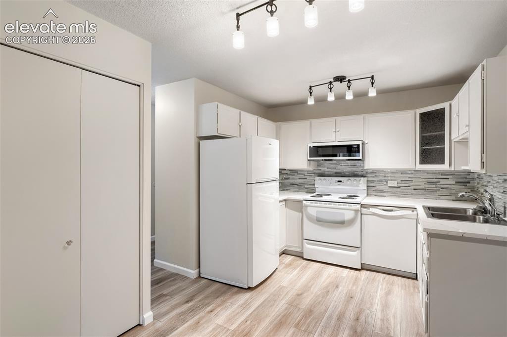 Image 25 of 27: Kitchen featuring wood-finish flooring, white cabinetry, and a mosaic tile