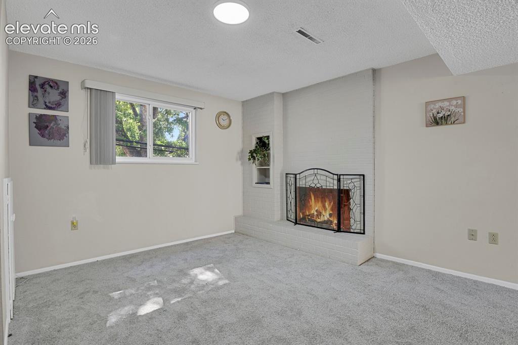 Image 12 of 31: Carpeted interior space featuring a white brick fireplace with a black meta