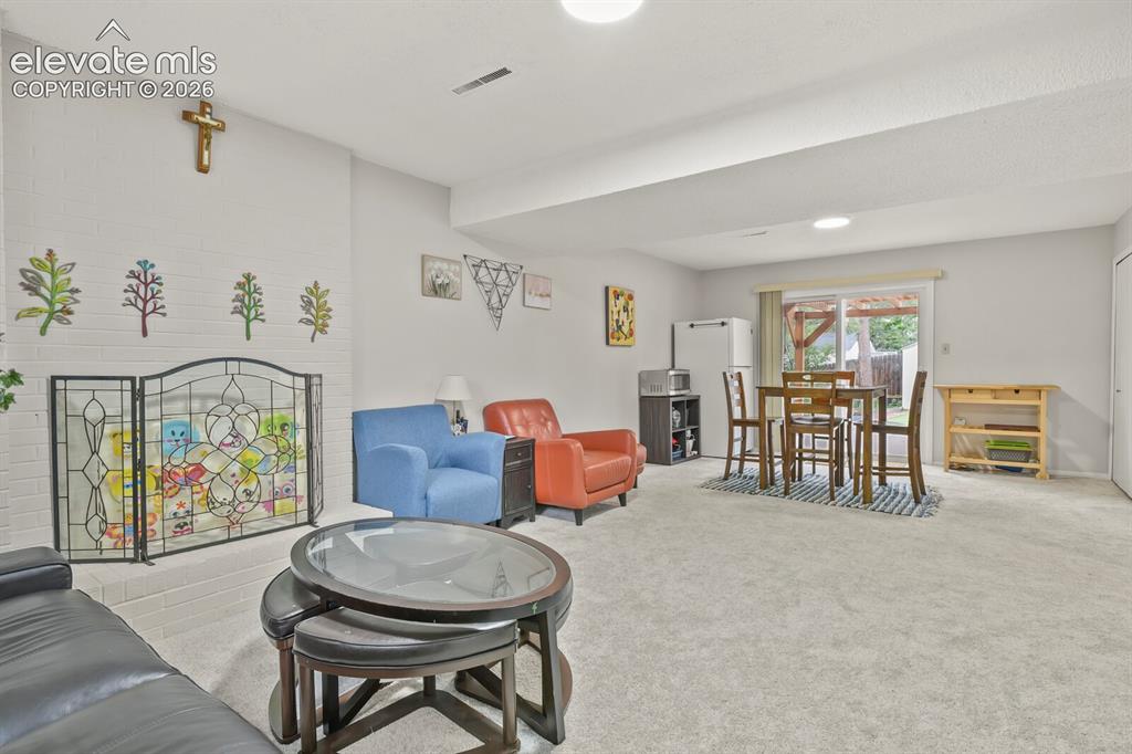 Image 25 of 39: Spacious carpeted room featuring a white brick fireplace with an ornate scr
