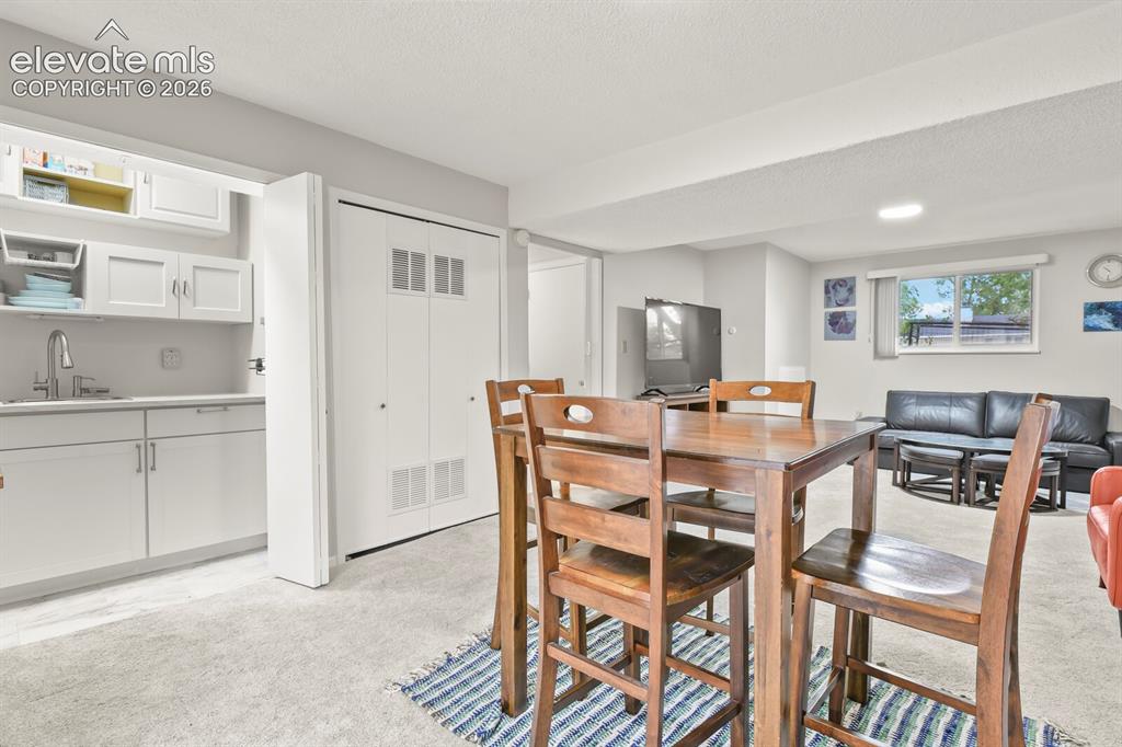 Image 32 of 39: Versatile lower-level space featuring a wet bar with white cabinetry and a 