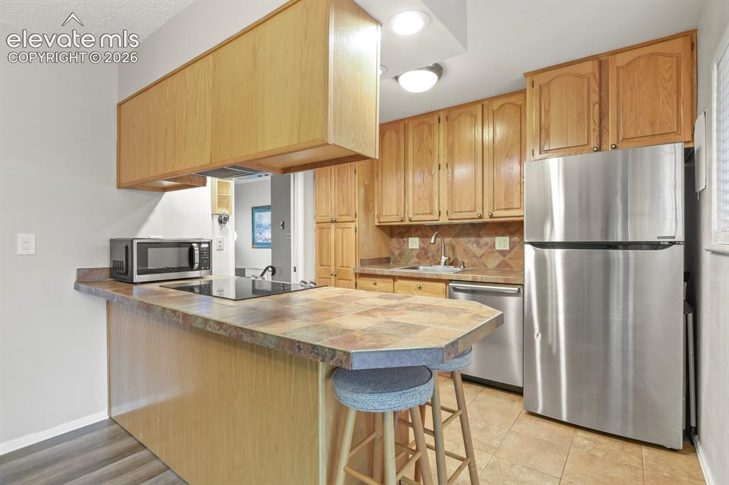 Image 7 of 31: Kitchen featuring wood cabinetry, stainless steel appliances, a tile counte