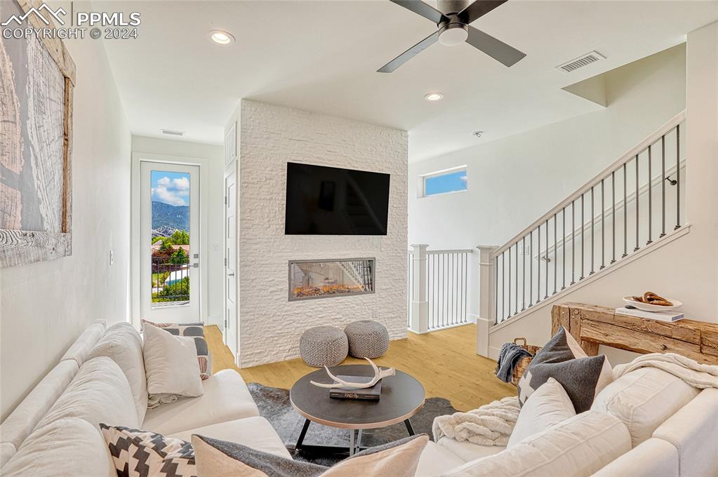 Image 6 of 24: Living room featuring a stone fireplace, ceiling fan, and hardwood / wood-s