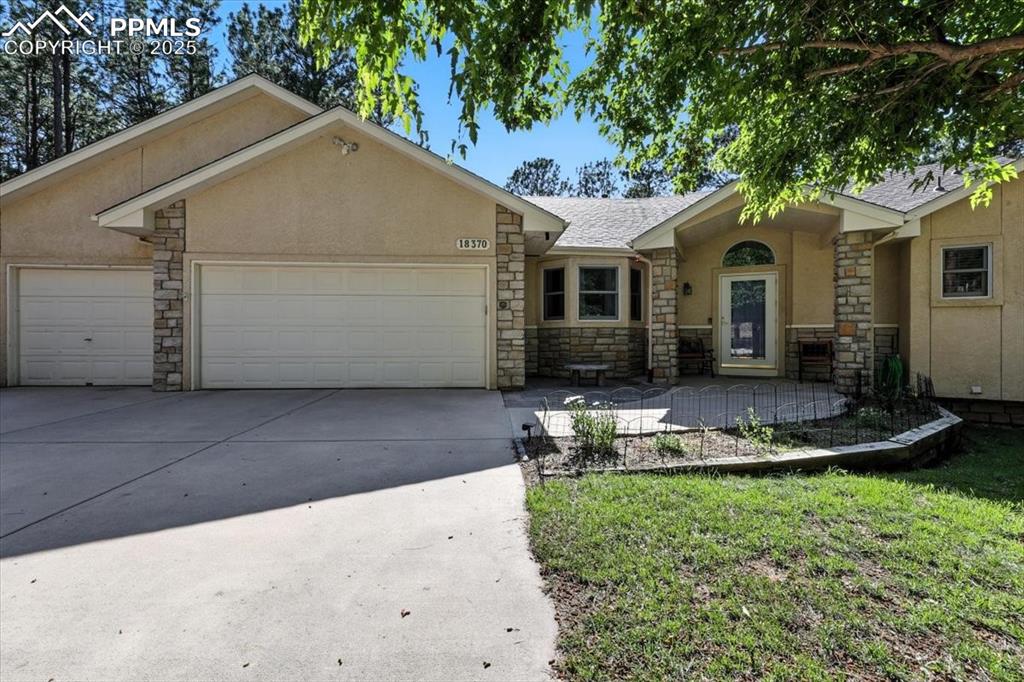 Caption: Single story home with stone siding, a garage, stucco siding, and driveway