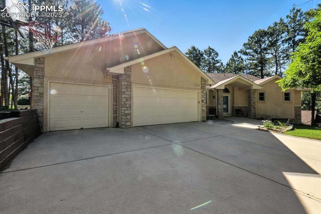 Image 2 of 45: View of front of home with stone siding, stucco siding, driveway, and a gar