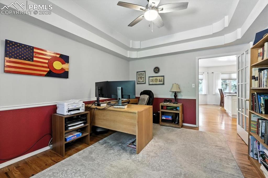 Image 26 of 45: Office space with wood finished floors, a raised ceiling, and ceiling fan