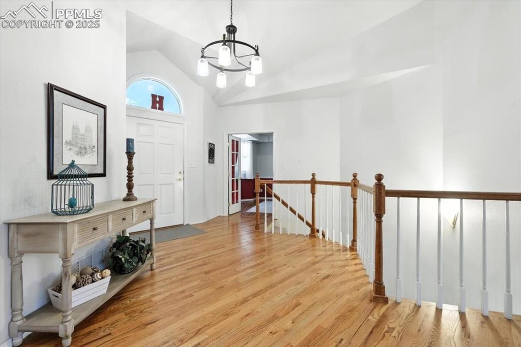 Image 7 of 45: Foyer with a chandelier, wood finished floors, and high vaulted ceiling