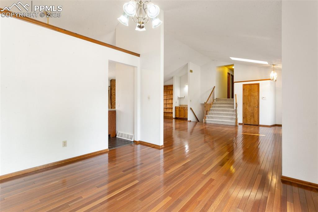 Image 10 of 30: Unfurnished living room with stairway, wood-type flooring, a chandelier, an