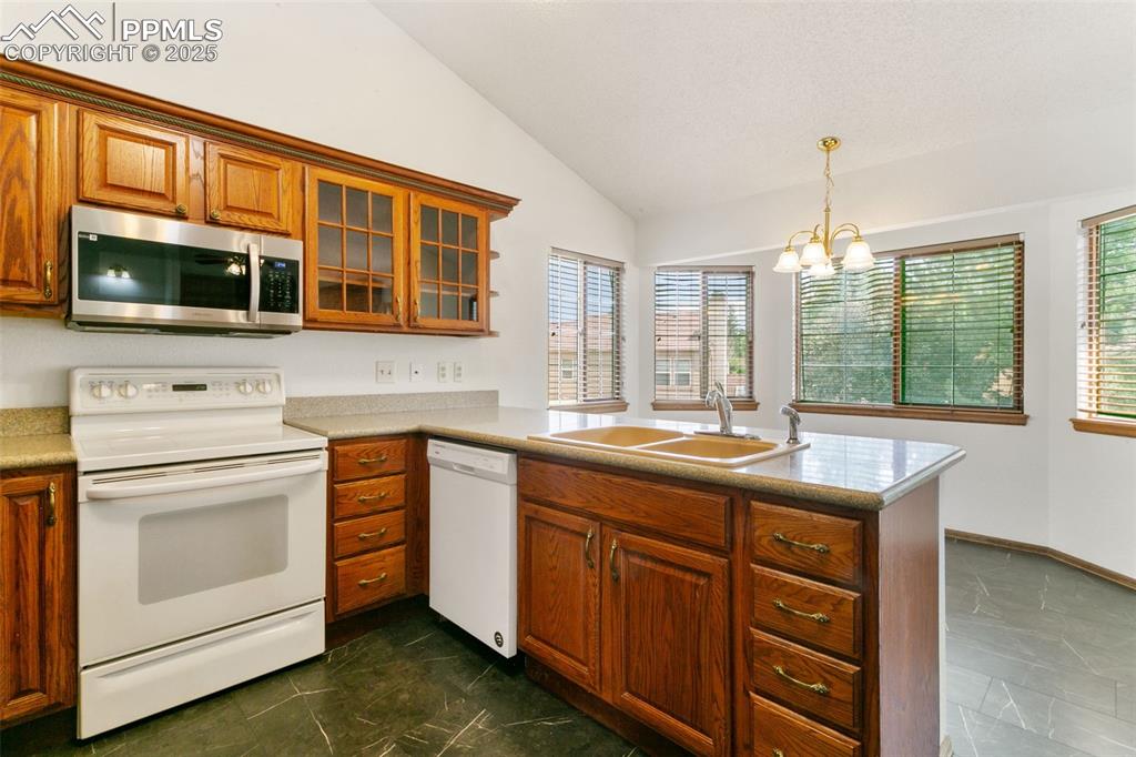 Image 11 of 30: Kitchen featuring white appliances, vaulted ceiling, brown cabinets, a chan