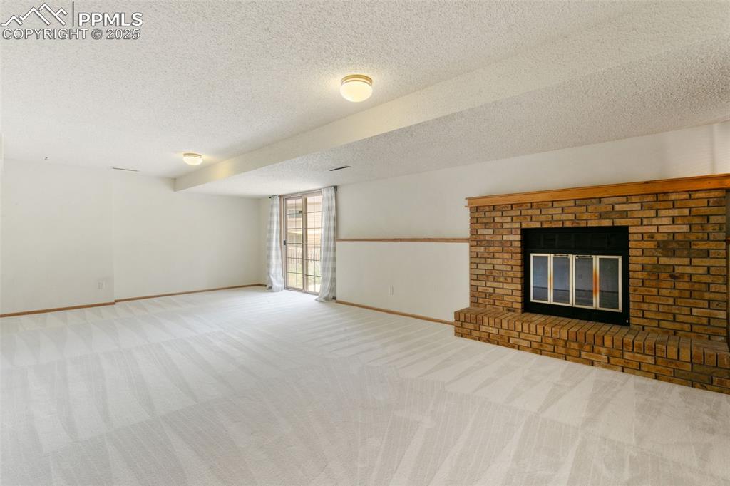 Image 24 of 30: Unfurnished living room with a textured ceiling, carpet floors, and a firep