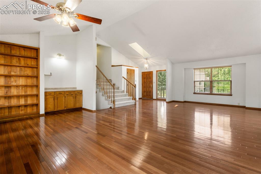 Image 7 of 30: Unfurnished living room with stairway, wood-type flooring, high vaulted cei