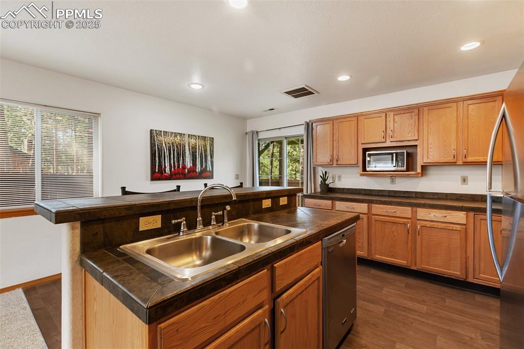 Image 9 of 30: Kitchen featuring an island with sink, dark wood-type flooring, tile counte
