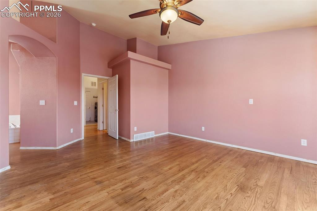 Image 15 of 34: Empty room with arched walkways, light wood-style floors, a ceiling fan, an