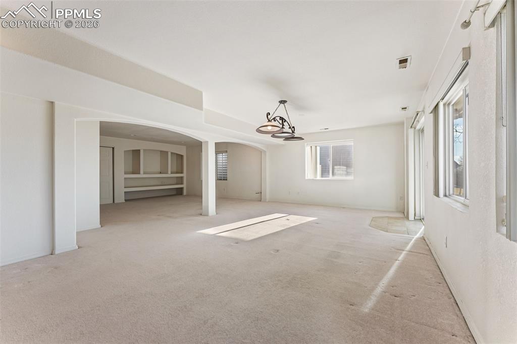 Image 25 of 34: Unfurnished living room with arched walkways and carpet flooring