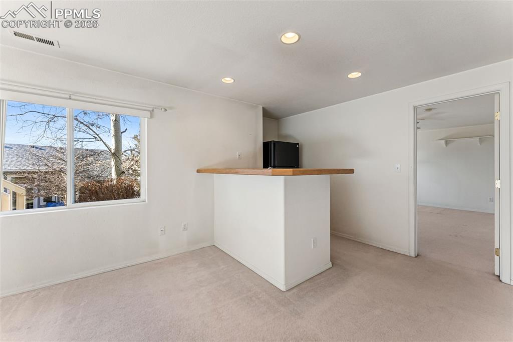 Image 29 of 34: Bar with light carpet, wooden counters, freestanding refrigerator, and rece