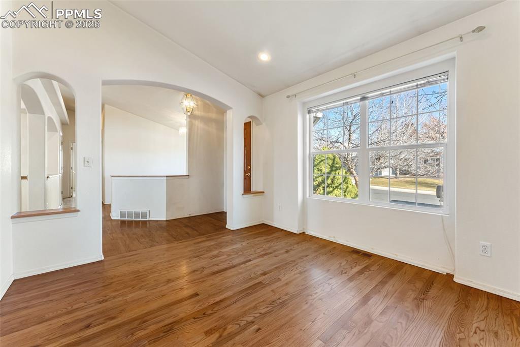 Image 3 of 34: Unfurnished room featuring vaulted ceiling, wood finished floors, arched wa