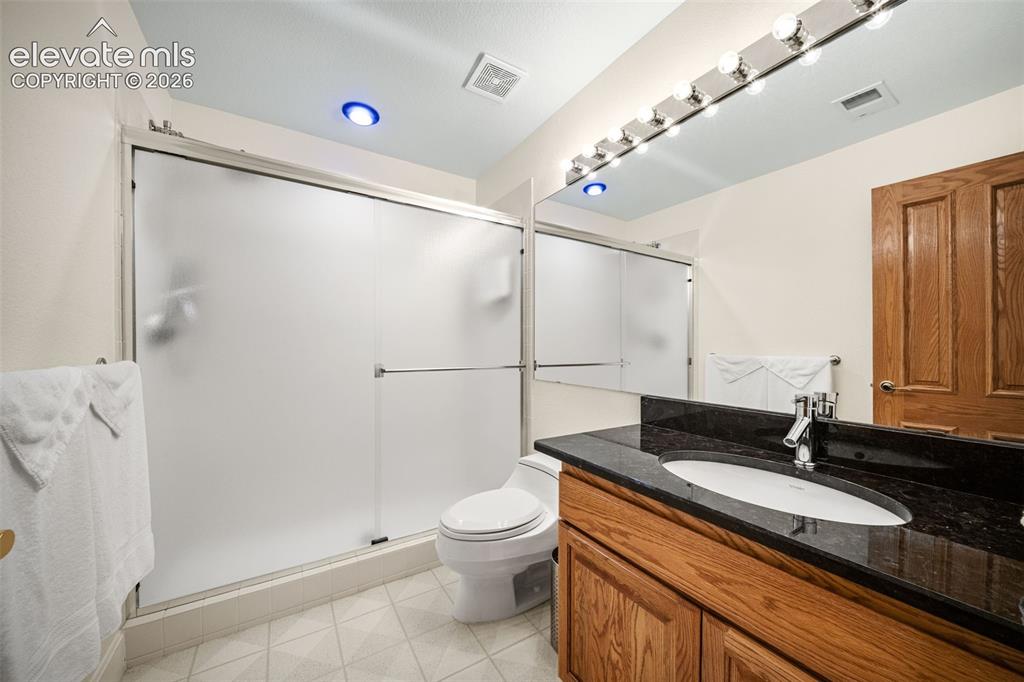 Image 32 of 50: Bathroom featuring an oak wood-finish vanity, dark stone countertop, and an