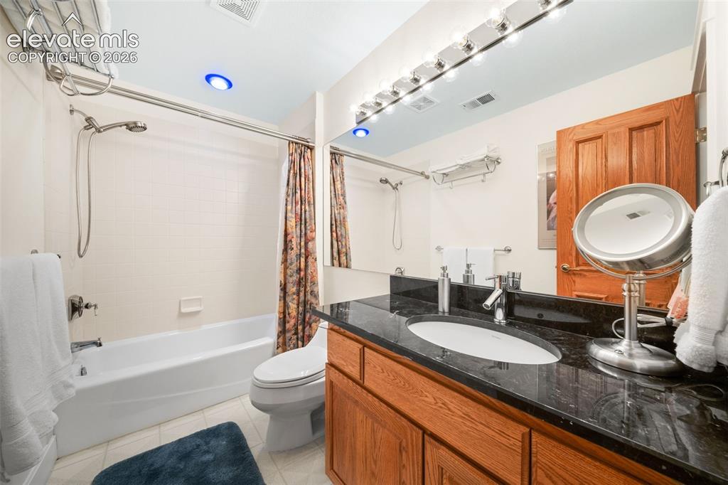 Image 34 of 50: Bathroom featuring a wood-finish vanity with a dark countertop and an under