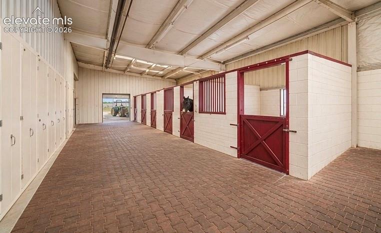 Image 41 of 50: Indoor equestrian facility featuring brick paver flooring, multiple horse s