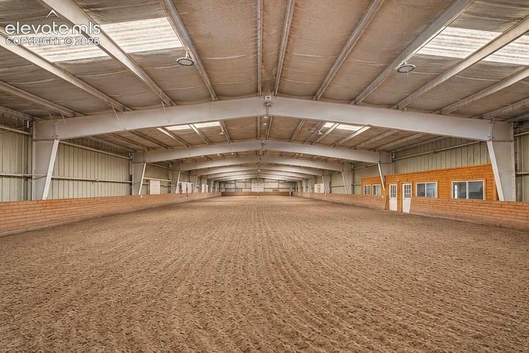 Image 42 of 50: Expansive indoor arena with a sand surface, brick-finish half-wall, and exp