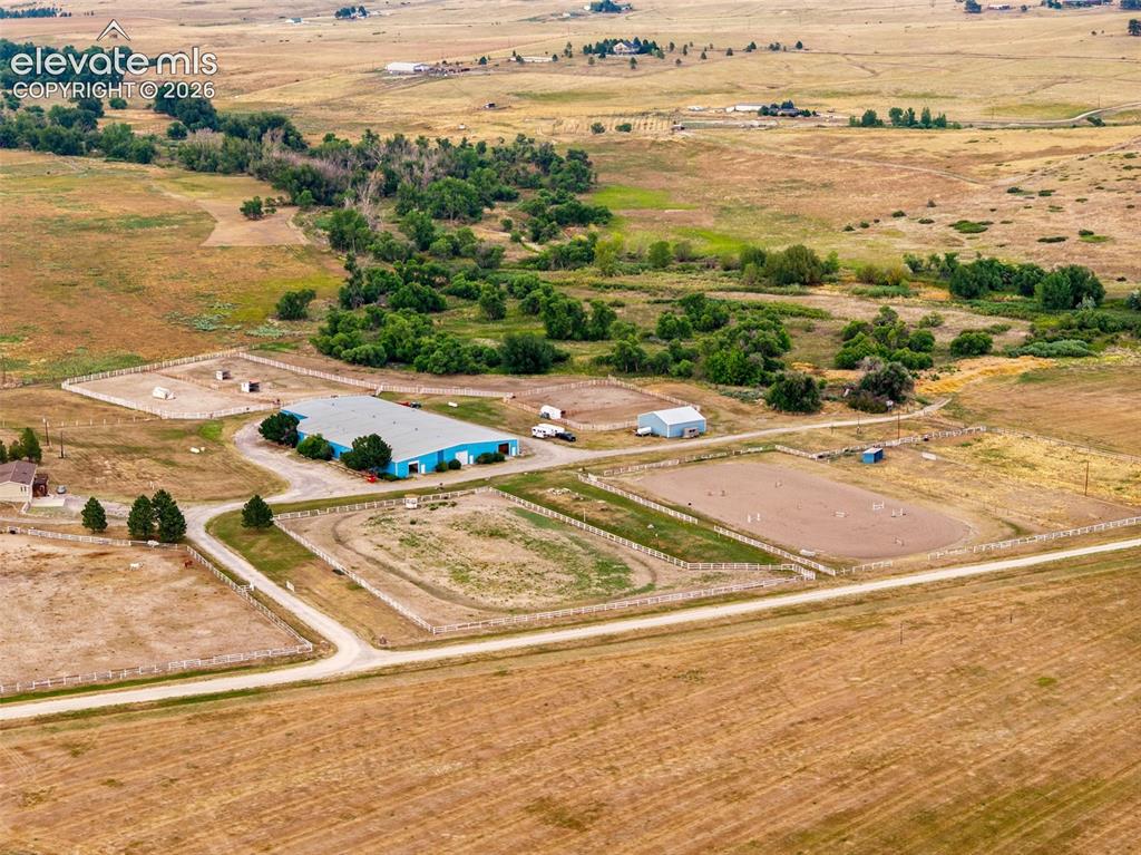 Image 46 of 50: Expansive acreage featuring multiple fenced paddocks, a large blue-roofed i
