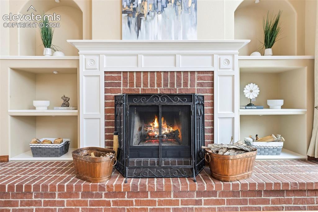 Image 16 of 50: Brick fireplace with a classic black metal screen, flanked by built-in shel